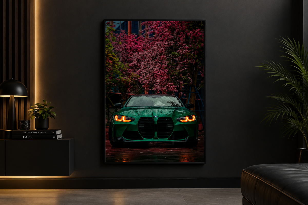 A framed vertical wall art print showing a green sports car with glowing headlights beneath pink flowering trees, displayed on a dark wall in a modern interior setting.