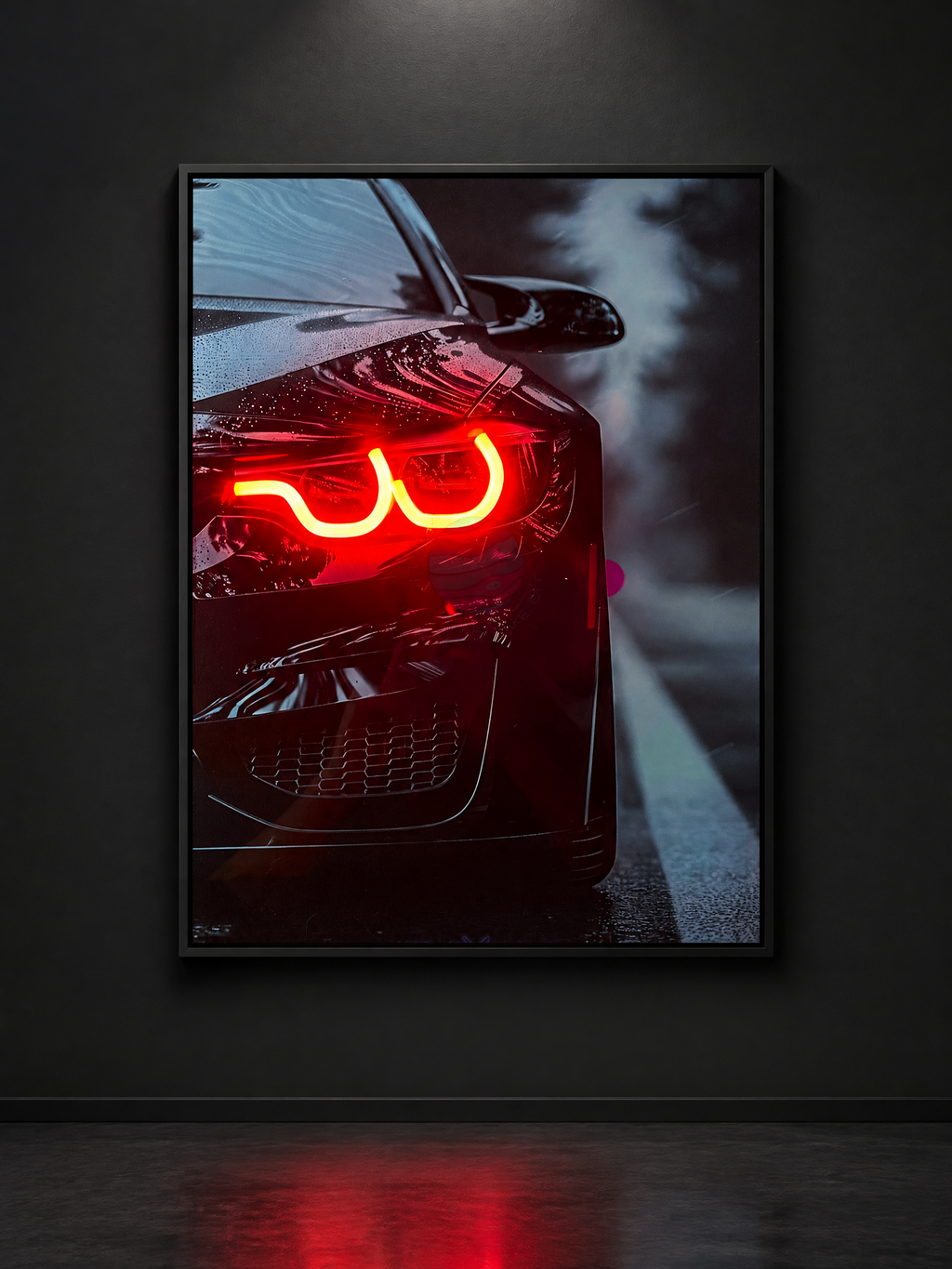 A framed wall art print showing a close-up of a black car with glowing red LED headlights, displayed against a dark gray wall with a reflective floor.