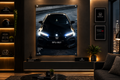 A large framed Honda car poster hangs on a dark wall in a modern living room. The poster shows a black Honda car with headlights on, and the room includes framed Honda logos on the right, shelving on the left, a sofa, and a city skyline visible at the window.