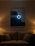 A framed Porsche car poster with a glowing blue ring light hangs on a warm brown wall above a beige sofa in a dimly lit living room.