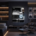 A framed wall art print depicting a close-up of a Mercedes-Benz G-Class vehicle front grille and headlights, displayed in a modern, dark-themed bedroom or lounge room with a leather chair, ottoman, shelving, and framed automotive photos.