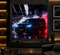 A large wall-mounted print or poster in a modern living room, showing a glossy black SUV on a wet city street at night with dramatic red and white lighting effects. The room includes a sofa, framed wall art, shelving, and a console table.