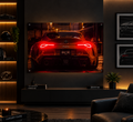 A framed wall art print showing the rear view of a red sports car with glowing taillights, displayed in a modern dimly lit living room above a console table.